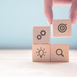 four wooden blocks with elements drawn on them: setting cogs, bullseye, light bulb and a magnifying glass.